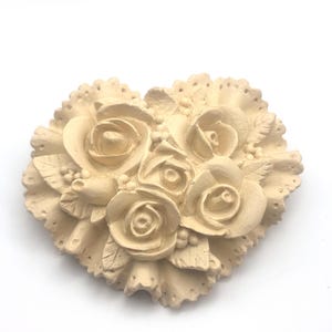 May include: A heart-shaped ceramic ornament with a raised design of beige roses and leaves.