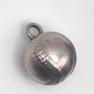 May include: A silver baseball charm with detailed stitching and a loop for attaching to a necklace or bracelet. The charm is a miniature replica of a baseball, perfect for sports enthusiasts.