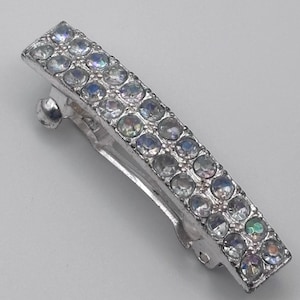 May include: Silver-toned rectangular hair clip adorned with two rows of iridescent, round rhinestones. The clip features a hinged design for secure attachment and is suitable for various hairstyles.