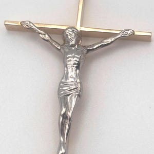 May include: A gold-toned crucifix with a silver-colored Jesus figure. The figure is depicted with outstretched arms on a cross. The cross has a vertical and horizontal beam, with the figure attached to the cross.