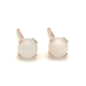 May include: A pair of small, white gemstone stud earrings with gold settings.