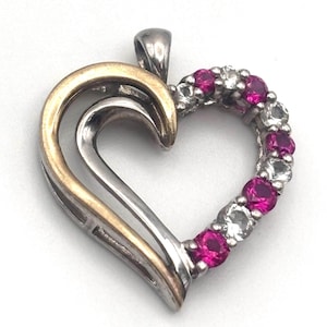 May include: A heart-shaped pendant with a gold and silver design. The right side of the heart is lined with alternating pink and clear gemstones. The pendant has a small loop at the top for a chain.