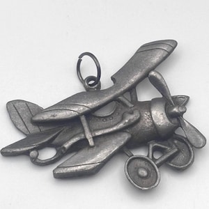 May include: A detailed, antique-style metal airplane charm with a propeller, wings, and wheels. The charm is silver-toned and features a loop for hanging. The biplane design evokes a vintage aesthetic, suitable for jewelry or craft projects.
