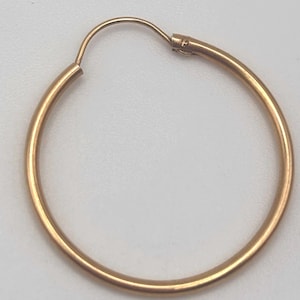 May include: A single gold hoop earring. The earring is a simple, circular design with a clasp closure. The hoop is approximately 1.5 inches in diameter and has a smooth, polished surface. The earring is set against a neutral background.