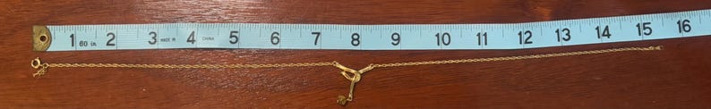 Pu&ograve; includere: Una collana a catena d'oro con un ciondolo a forma di chiave, misurata con un righello, che mostra che &egrave; lunga circa 30 cm.