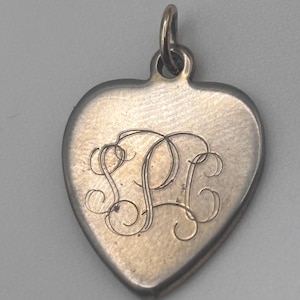 May include: Silver heart-shaped charm with a monogram of the letters "SPC" engraved in a cursive script.