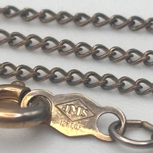 May include: Close-up of a vintage gold-tone chain necklace. The chain has a delicate, textured design with a lobster clasp. The clasp is stamped with "JMS" and "12K.G.F."