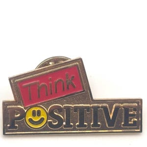 May include: Gold-colored pin with a red rectangle that says "Think" and a gold rectangle that says "POSITIVE" with a yellow smiley face.