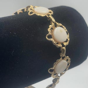 May include: Gold tone bracelet with three oval shaped white mother of pearl stones set in ornate gold tone frames.