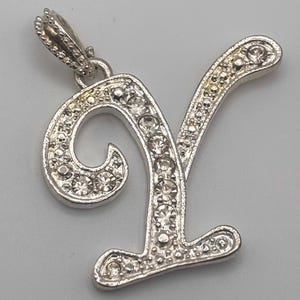 May include: Silver-toned pendant in the shape of the letter "Y", encrusted with clear, sparkling rhinestones. The pendant has a decorative bail for attaching to a chain. The design is elegant and suitable for jewelry.