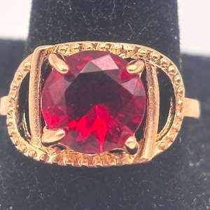 May include: A gold ring with a large, round, red gemstone.