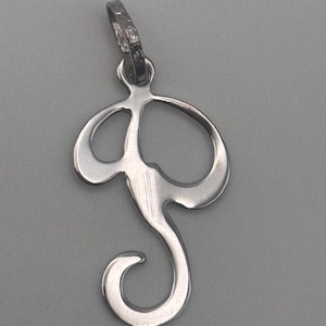May include: A silver pendant in the shape of the letter "S". The pendant has a loop at the top for a chain and a stylized, cursive design. The metal has a polished finish, reflecting light.
