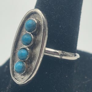 May include: A silver ring with an oval shaped band featuring five turquoise stones set in a row.
