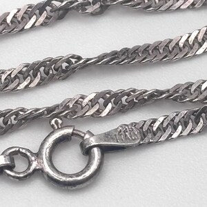 May include: Close-up of a silver-colored necklace with a twisted rope chain design. The necklace has a lobster clasp closure. The clasp is marked with "925 Italy". The chain is approximately 0.2 inches wide.