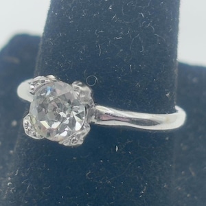 May include: A silver ring with a clear, round, faceted gemstone set in a prong setting.