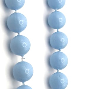 May include: Close-up of a light blue beaded necklace. The beads are round and evenly spaced, strung together with white string. The necklace is against a white background.