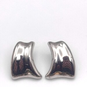 May include: A pair of silver-toned metal earrings with a smooth, polished, and reflective surface. Each earring features a curved, asymmetrical, and tapered shape that widens toward the base, creating a sleek and solid appearance for the jewelry.