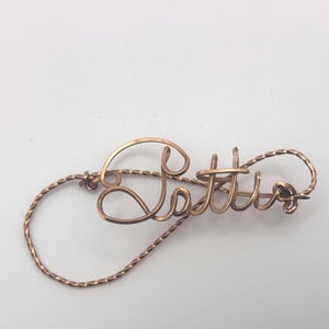 May include: A copper wire name pin with the word "Lottie" spelled out in cursive.