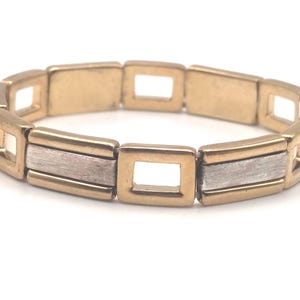 May include: A gold bracelet with a two-tone design. The bracelet is made of linked squares with alternating gold and silver finishes.