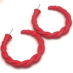 May include: A pair of red hoop earrings with a twisted rope design. The earrings are a vibrant shade of red and have a post closure. The hoops are a medium size and are set against a white background.