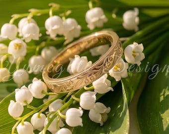 May include: A gold band ring featuring an engraved floral pattern resting on a cluster of white lily of the valley flowers with green leaves. The image includes the text "Yusmegi Design" and "BLACK FRIDAY 30% OFF" with a heart icon.
