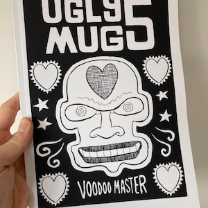 May include: Black and white illustration of a cartoon face with the text "Ugly Mug Voodoo Master" above it. The face has a heart on its forehead, a large nose, and a wide, toothy grin.