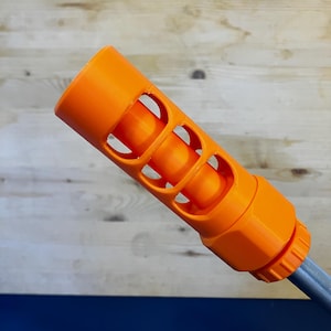 May include: Bright orange cylindrical object with three curved cutouts, attached to a gray tube. The object has a textured surface and a threaded end. The background is a mix of wood and blue.