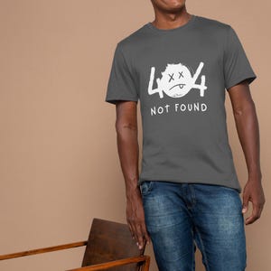 Op de afbeelding: Een grijs t-shirt met de tekst "404 NOT FOUND" in het wit. De afbeelding toont een ongelukkig, verdrietig gezicht. De persoon op de foto draagt een blauwe spijkerbroek.