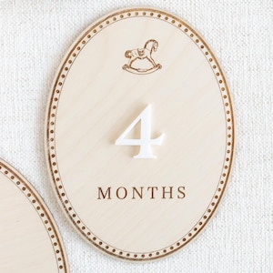 Close-up of engraved wooden baby month milestone plaque with teddy bear artwork and clean neutral finish. Baby monthly photo prop for newborn milestones and infant monthly pictures, used to show baby age 1 month, 2 months, 3 months and beyond. Great for first year photo keepsakes, baby shower gift, neutral nursery decor, wooden month markers, milestone discs/plaques.