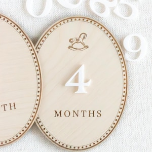 Handmade wooden baby milestone markers used as monthly photo props for newborn and infant pictures. Teddy bear themed month plaques highlight baby age and first year milestones from 1 month to 12 months. Neutral nursery decor for baby boy or gender neutral spaces, ideal baby shower gift and keepsake for first year baby photos.