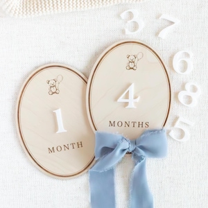 Set of wooden monthly milestone plaques for baby photos, designed to document baby growth from newborn to one year. Baby month markers used in monthly photo sessions, flat lays, and nursery styling. Neutral teddy bear design fits modern nursery decor, baby boy milestone photos, gender neutral baby gifts, handmade wooden milestone discs or plaques.