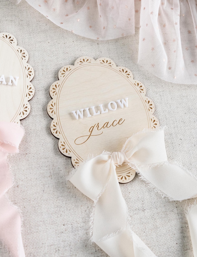 Lace Frame Milestone Marker with Scallop Border. Coquette Bow Detail with block font first name and script middle name or last name or both. Each Lace Frame is adorned with a silk chiffon ribbon in the color light pink or ivory. White acrylic milestone markers with the monthly number interchangeable in acrylic. Matching lace Frame name plate that can be used as a newborn hospital announcement. Milestone marker for girl, bow milestone card for girl, hospital name announcement for girl, wooden