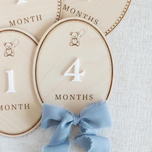 Wooden baby milestone plaques designed for monthly baby photos, featuring a soft neutral teddy bear theme. Used as baby month markers to capture newborn through first year milestones from 1 month to 12 months. Ideal photo prop for infant pictures, baby boy or gender neutral nursery decor, first year baby keepsake, baby shower gift, handmade wooden milestone discs or plaques.