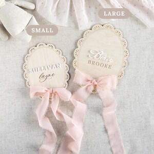 Lace Frame Milestone Marker with Scallop Border. Coquette Bow Detail with block font first name and script middle name or last name or both. Each Lace Frame is adorned with a silk chiffon ribbon in the color light pink or ivory. White acrylic milestone markers with the monthly number interchangeable in acrylic. Matching lace Frame name plate that can be used as a newborn hospital announcement. Milestone marker for girl, bow milestone card for girl, hospital name announcement for girl, wooden