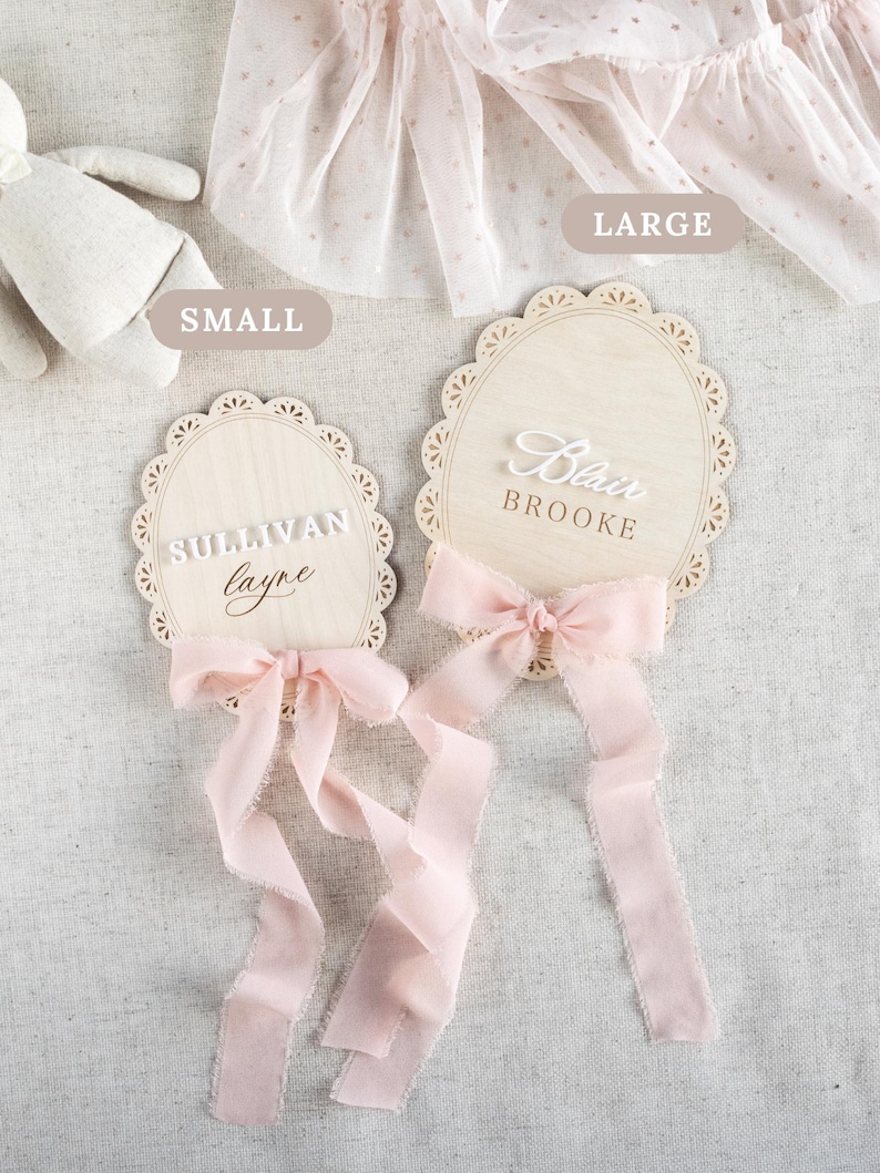 Lace Frame Milestone Marker with Scallop Border. Coquette Bow Detail with block font first name and script middle name or last name or both. Each Lace Frame is adorned with a silk chiffon ribbon in the color light pink or ivory. White acrylic milestone markers with the monthly number interchangeable in acrylic. Matching lace Frame name plate that can be used as a newborn hospital announcement. Milestone marker for girl, bow milestone card for girl, hospital name announcement for girl, wooden