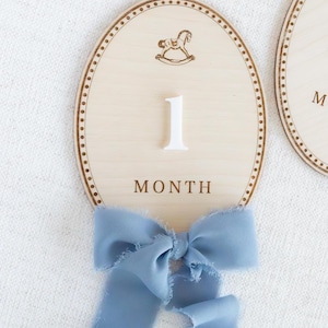 Handmade wooden baby milestone markers used as monthly photo props for newborn and infant pictures. Teddy bear themed month plaques highlight baby age and first year milestones from 1 month to 12 months. Neutral nursery decor for baby boy or gender neutral spaces, ideal baby shower gift and keepsake for first year baby photos.