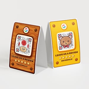 以下が含まれることがあります： GoogleのロゴとQRコードが付いた2つの卓上カード。1つはキノコのグラフィック、もう1つはクマのグラフィックで、どちらも「LEAVE US A REVIEW ON GOOGLE！」というテキストが入っています。