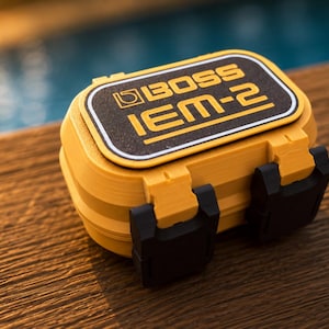 Könnte beinhalten: Gelb-schwarzes BOSS IEM-2 In-Ear-Monitor-System. Der rechteckige Koffer hat ein schwarz-gelbes Etikett mit dem BOSS-Logo und dem Text IEM-2. Der Koffer hat schwarze Verschlüsse.