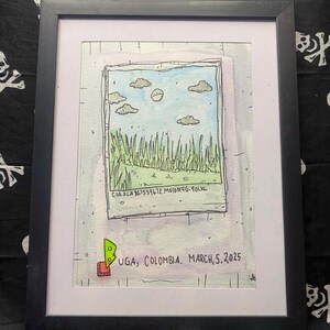 May include: A framed illustration featuring a hand-drawn polaroid-style image of a grassy field under a blue sky with clouds and a sun. The print includes the text "CIA-FLA 861539672 M010019G-90LXL" and "BUGA, COLOMBIA. MARCH, 5. 2025" with a small green and red icon.