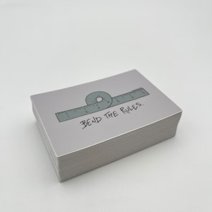 May include: A stack of gray stickers with a ruler and a circle drawn around it. The text "BEND THE RULES." is written below the ruler.