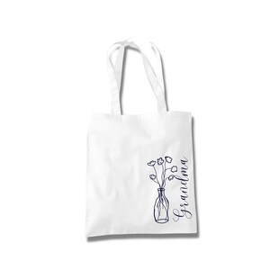 Pu&ograve; includere: Borsa tote bianca con un disegno a linea blu di un vaso di fiori e la parola "Nonna" scritta verticalmente sul lato destro.
