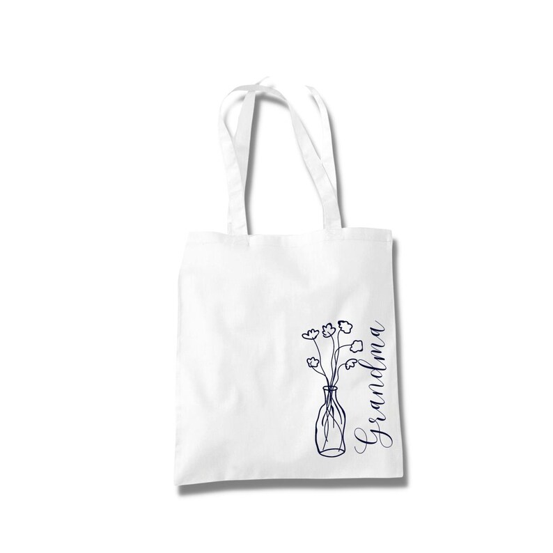 Pu&ograve; includere: Borsa tote bianca con un disegno a linea blu di un vaso di fiori e la parola "Nonna" scritta verticalmente sul lato destro.