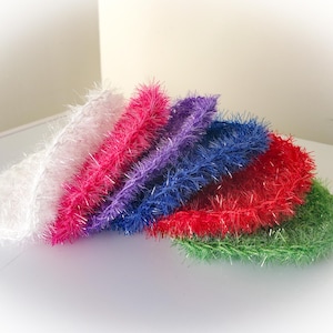 May include: A collection of colorful, round, fluffy scrubbies in white, pink, purple, blue, red, and green. These textured items are arranged in a fan shape, showcasing their vibrant hues and soft, fuzzy appearance.