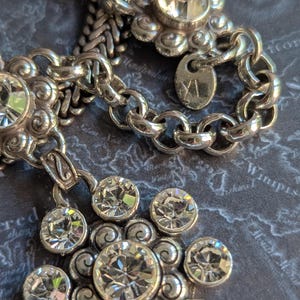 Peut inclure: Collier argent&eacute; avec un pendentif floral et des cristaux transparents &eacute;tincelants. Le collier pr&eacute;sente un motif de cha&icirc;ne et une petite &eacute;tiquette. Le pendentif a un grand cristal central entour&eacute; de petits cristaux.