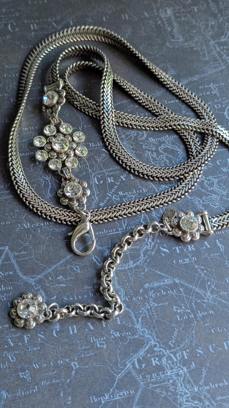 Peut inclure: Collier argent&eacute; avec un pendentif floral et des accents de cristaux transparents. Le collier pr&eacute;sente un motif de cha&icirc;ne tiss&eacute;e et une fermeture &agrave; mousqueton. Le pendentif comporte plusieurs cristaux transparents dispos&eacute;s en forme de fleur.