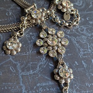 Peut inclure: Collier argent&eacute; orn&eacute; de plusieurs pendentifs en forme de fleurs, chacun orn&eacute; de strass clairs et &eacute;tincelants. Le collier est dot&eacute; d'une cha&icirc;ne tress&eacute;e et d'un fermoir mousqueton. Le fond est une carte sombre.
