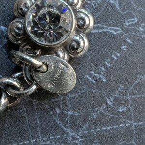 Peut inclure: Gros plan sur un bracelet argent&eacute; avec une grosse pierre pr&eacute;cieuse ronde et transparente sertie dans un motif floral. Le bracelet a une cha&icirc;ne et une petite &eacute;tiquette avec l'inscription "TAIWAN". Le fond est une surface gris fonc&eacute; avec un motif de carte.