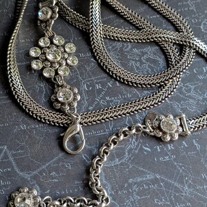 Peut inclure: Collier argent&eacute; avec un pendentif floral et des cristaux transparents &eacute;tincelants. Le collier pr&eacute;sente un motif de cha&icirc;ne et un fermoir mousqueton. Le pendentif est en forme de fleur avec plusieurs cristaux. Le collier est pr&eacute;sent&eacute; sur un fond gris fonc&eacute;.