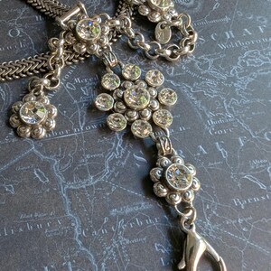 Peut inclure: Collier argent&eacute; orn&eacute; de pendentifs en forme de fleurs et de cristaux transparents. Le collier pr&eacute;sente un motif de cha&icirc;ne et une fermeture &agrave; mousqueton. Le bijou est pr&eacute;sent&eacute; sur une surface bleu fonc&eacute; &agrave; motif de carte.