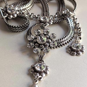 Peut inclure: Collier argent&eacute; avec un pendentif floral et des accents de cristaux transparents. La cha&icirc;ne est tress&eacute;e et se ferme avec un fermoir mousqueton. Le design comprend un anneau et un petit pendentif fleur.